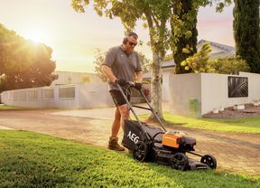 Person mowing a lawn in a well-maintained suburban garden during golden-hour light.