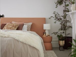 Bedroom with a large indoor plant, white lamp on side table, cushions, and white bedding