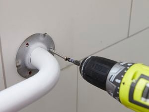 Drilling a screw into a grab rail bracket on a tiled wall