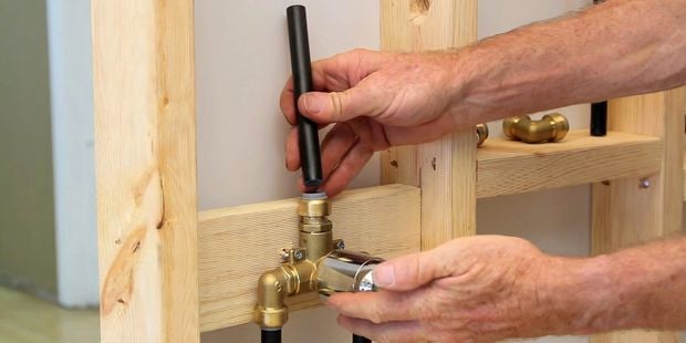 A person fitting a black tube to a brass tee.