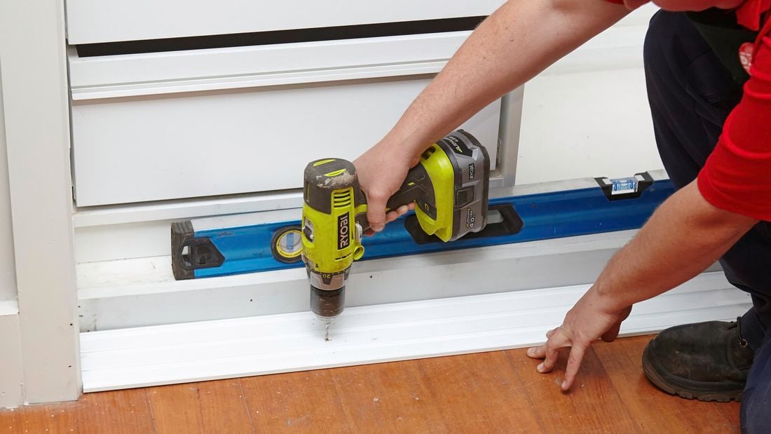 A person fixing a base plate timber to the floor using a cordless driver