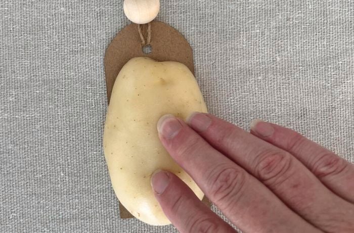 Hand presses potato stamp onto cardboard tag