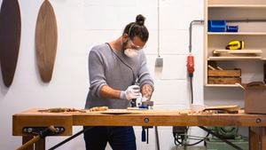 Man using a rotary tool to carve wood, with 2 wooden surfboards hanging on the wall in the background