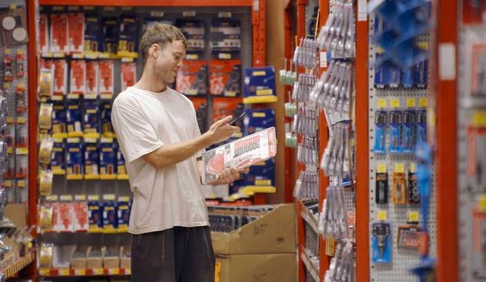 Customer in aisle in the tool shop looking at product and mobile phone