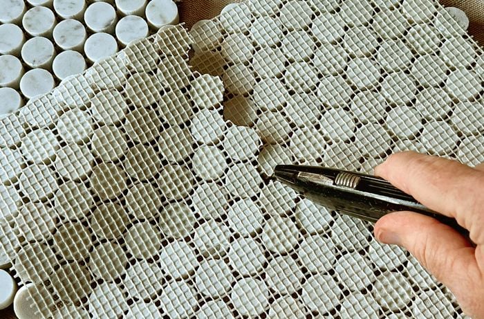 A utility knife is used to cut the mesh on the back of a mosaic tile sheet.