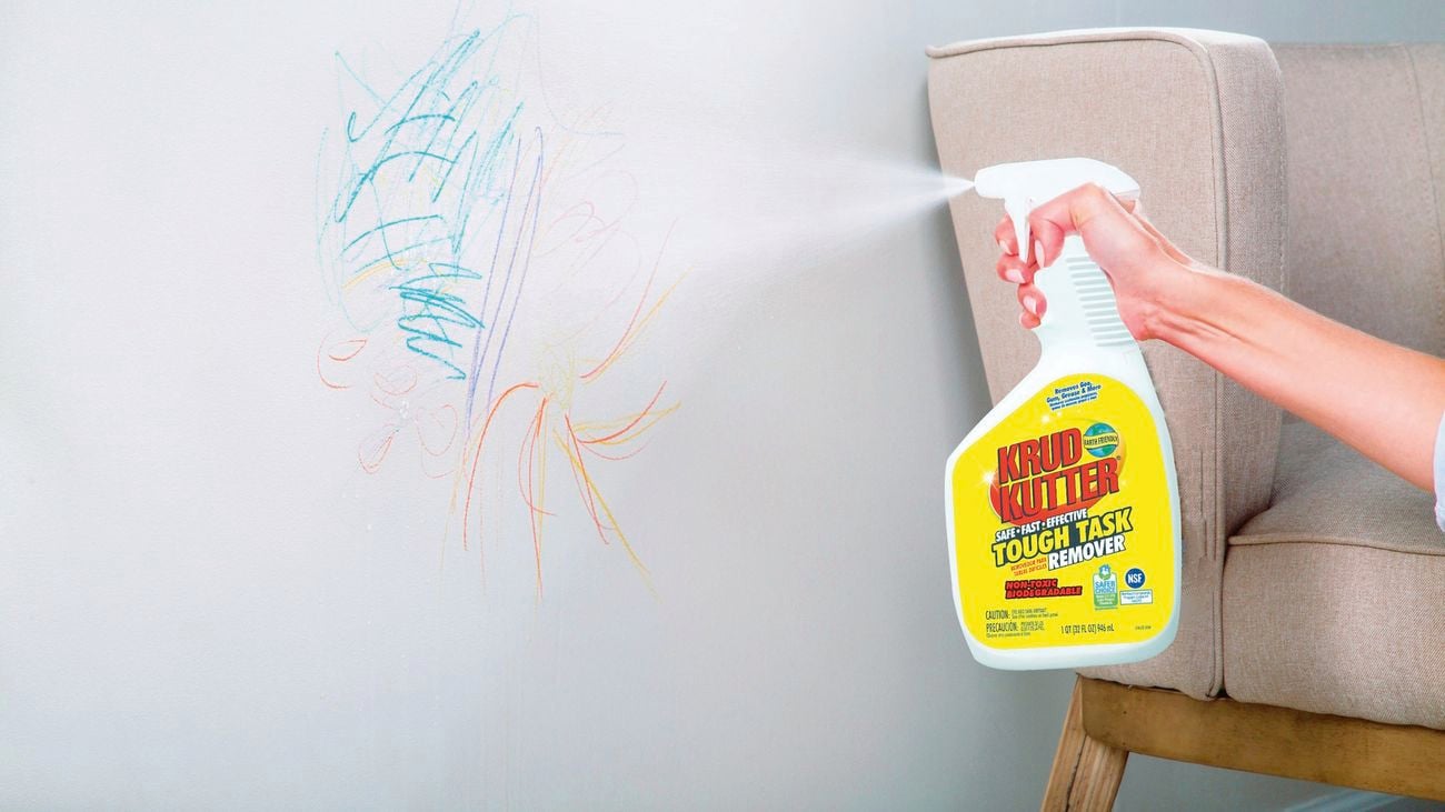 Hand uses Krud Kutter spray bottle to spray paints on white wall
