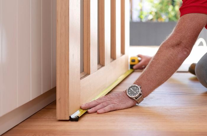 A person in a red T-shirt measures the door bottom with a measuring tape.