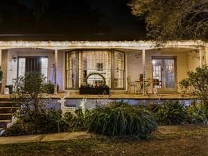  Outdoor Christmas display with a large wreath in a planter, string lights on windows, and illuminated reindeer and star decorations in the garden.
