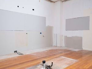 The image shows a completely stripped kitchen space with drywall patches and exposed flooring.