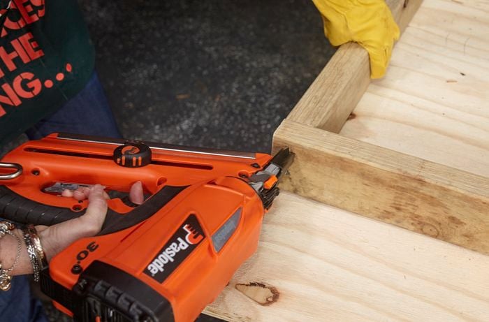 A nail gun being used to assemble a wooden bed frame