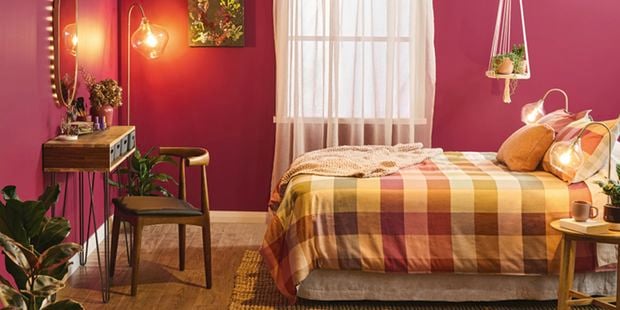 Moody bedroom with dark pink walls, timber furniture and styled bed.