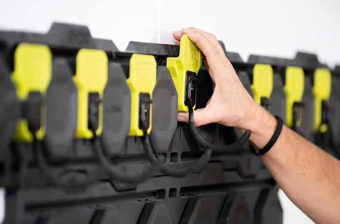 A person is attaching a yellow Ryobi LINK hook onto the installed wall rail system for garden tools, extension cords or even ladders.  