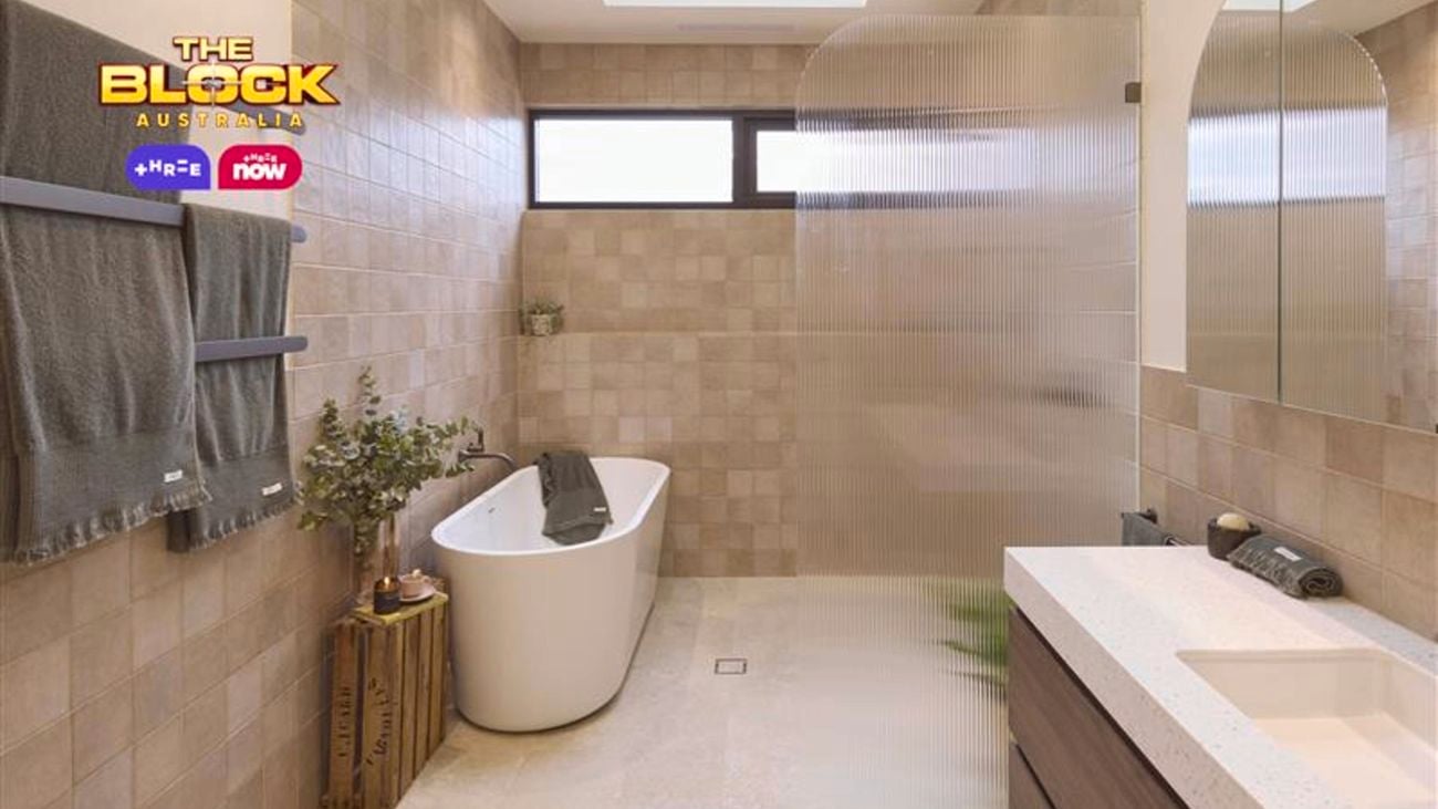 Light brown bathroom with a bath, plants, shower screen, white vanity with brown drawers underneath it and tiled floors in it.