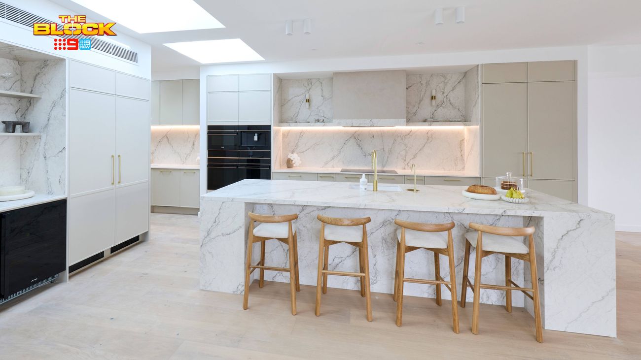 Contemporary kitchen featuring a marble-look island bench with timber bar stools, neutral cabinetry, skylights and integrated appliances.