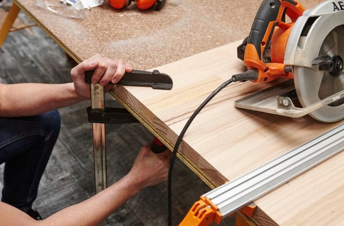 A person clamping a panel of timber to a work bench