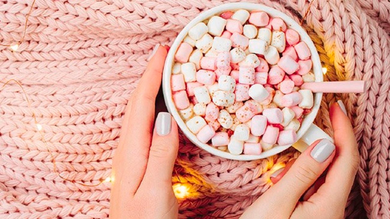 A hot drink with marshmallows on top of a pink throw and wire lights.