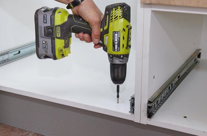 A person inserting a screw through the bottom of a cabinet into the kickboard