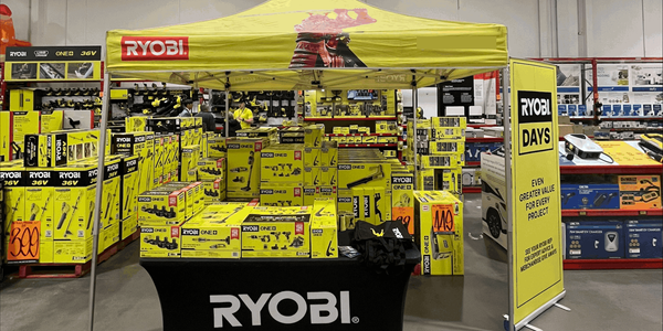 A Ryobi Days promotional booth inside a Bunnings Warehouse featuring a yellow Ryobi canopy, product displays, and branded signage.