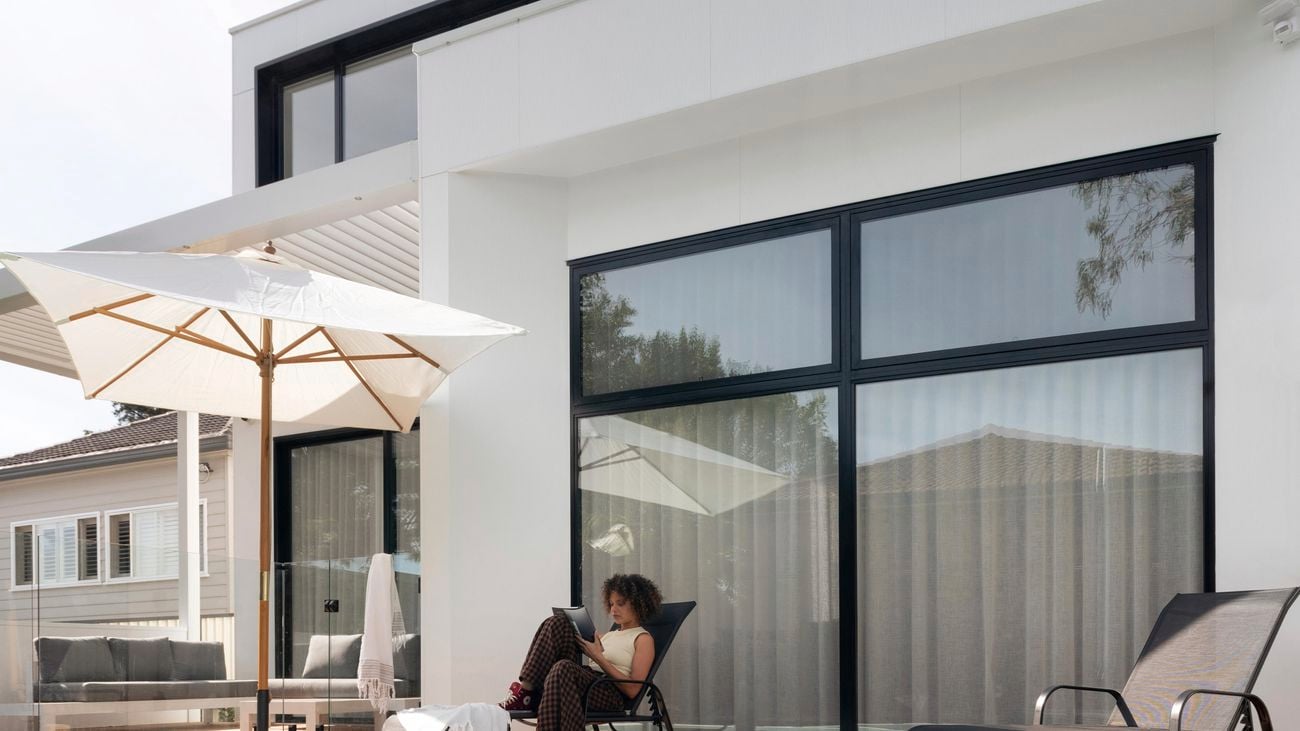 After picture of home, a backyard view of white exterior house and a woman sitting by the pool.