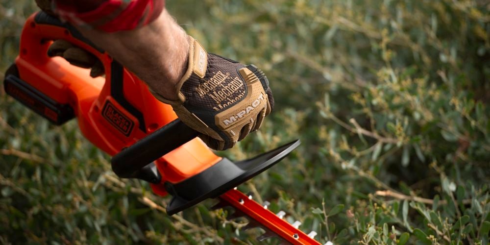 Person trimming the hedges with a hedge trimmer and wearing protective gloves