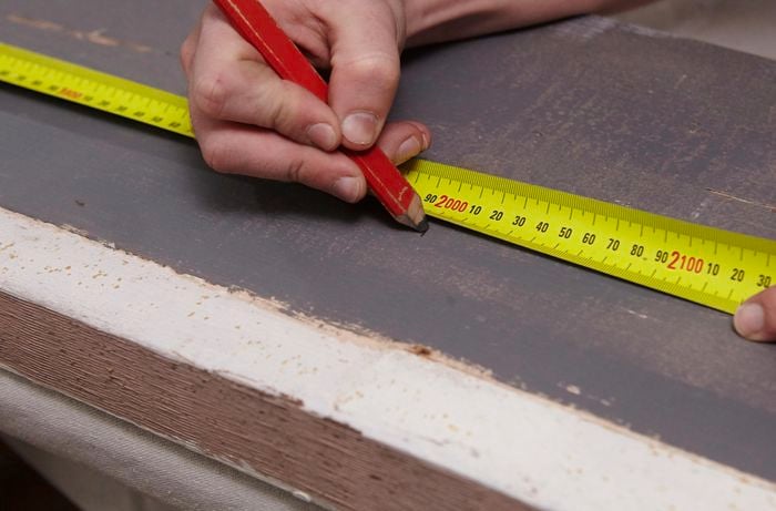 A person marking 2 metres on a length of recycled timber using a measuring tape