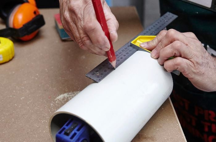 A person attaching a length of PVC pipe to a timber shelving unit using a cordless drill