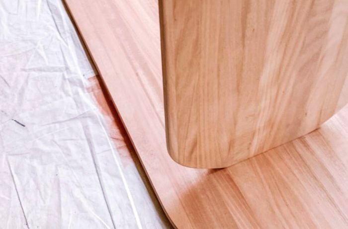 Curved plank of wood standing upright on longer plank of wood lying flat on ground to form legs.
