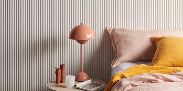 Pink and white Laminex wall in a bedroom with bed and side table.