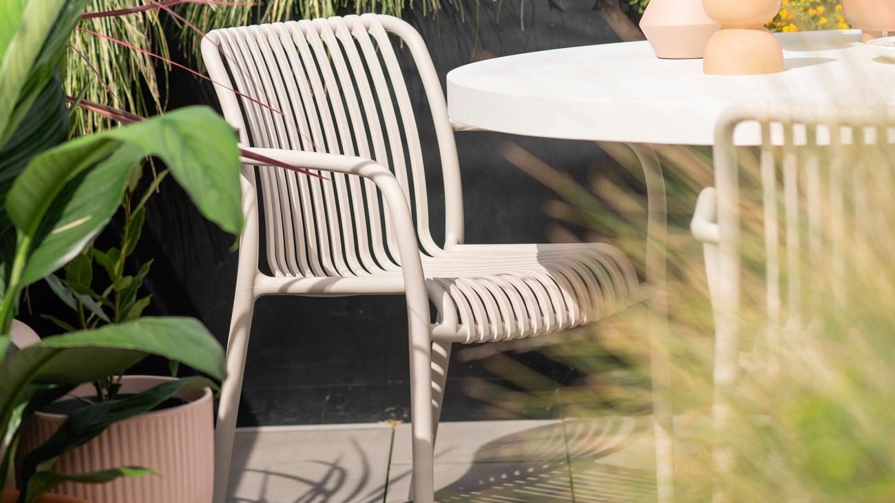White outdoor table with one chair, outside with pot plants.