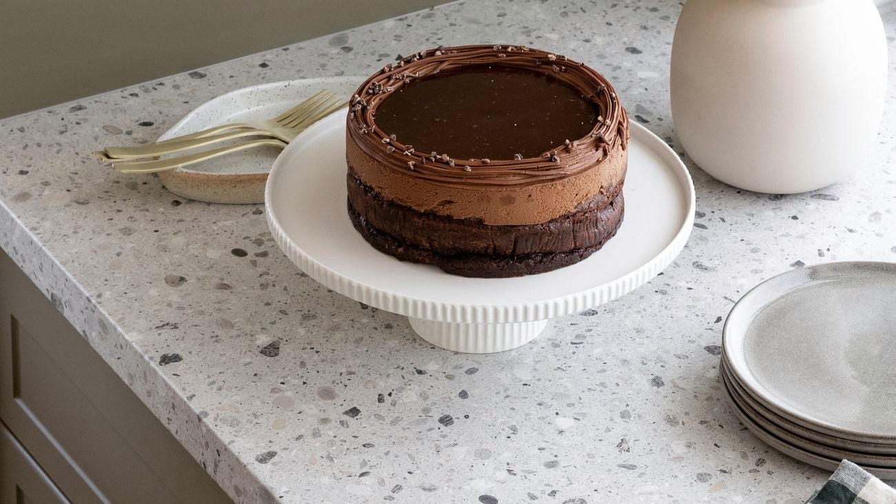 Speckled grey granite benchtop with plates, cutlery, a chocolate cake on a cake stand and a pot plant on top