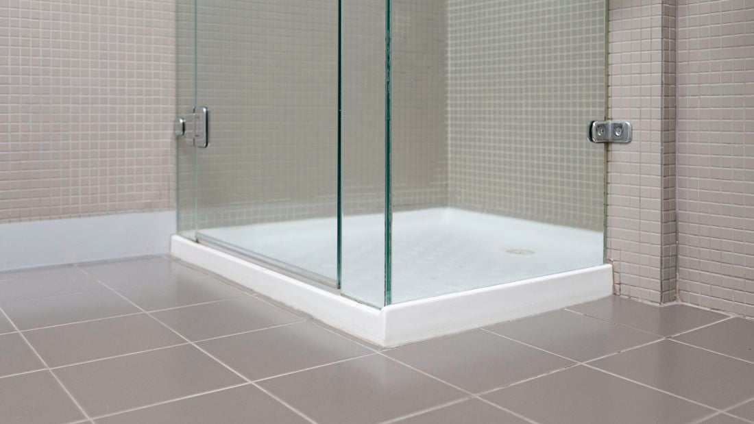 A shower with a glass door in a bathroom with tiles on the walls.