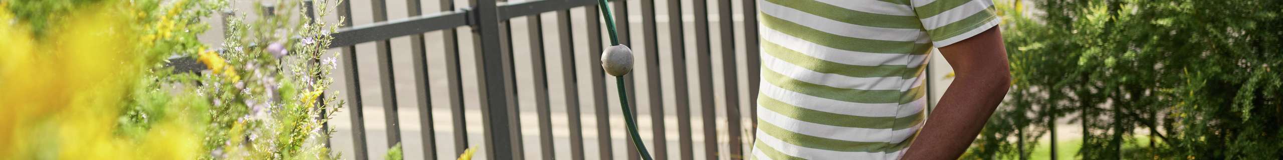 Person using a garden hose to water flowering plants in a front garden.