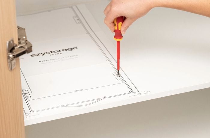 A person is using a paper template to guide the placement of fixing holes and ensure the drawer system is installed correctly.