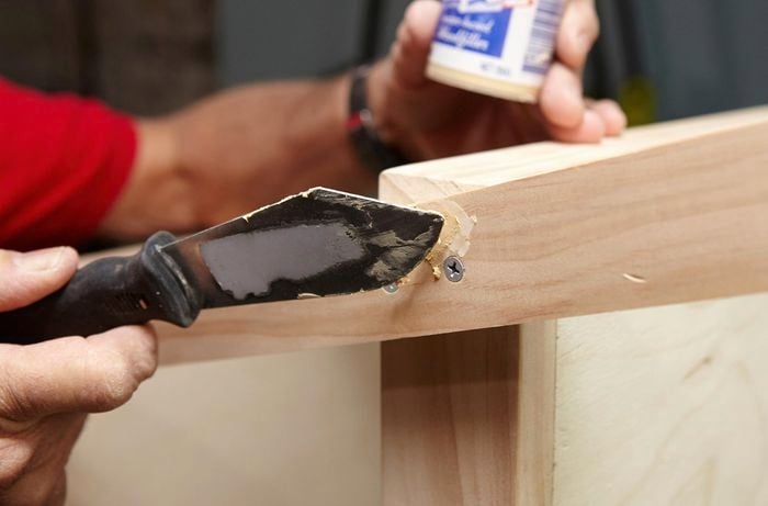 A person filling screw heads with wood filler using putty knife