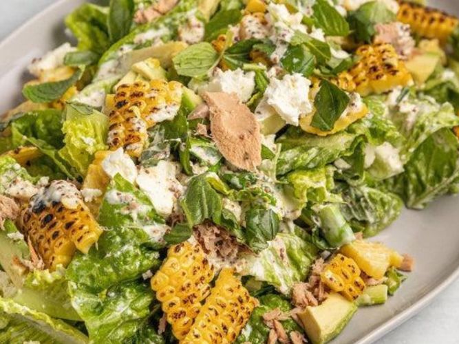Fresh salad with grilled corn, avocado, tuna, crumbled cheese and herbs, dressed with a creamy sauce in a serving bowl.