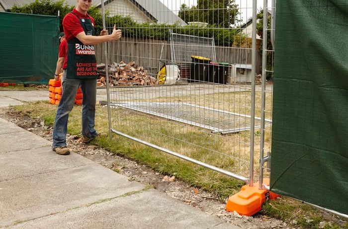 A person holding a length of temporary fencing with one end in a concrete block