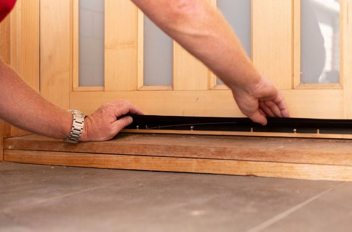 A person is sliding the weather strip seal over the screws.