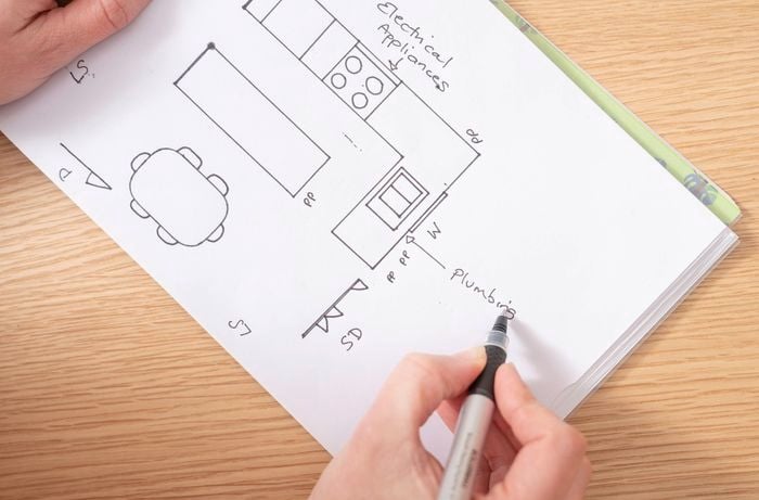 A person is marking services like plumbing, power points, windows, and sliding doors in a hand-drawn kitchen floor plan for accurate layout planning.