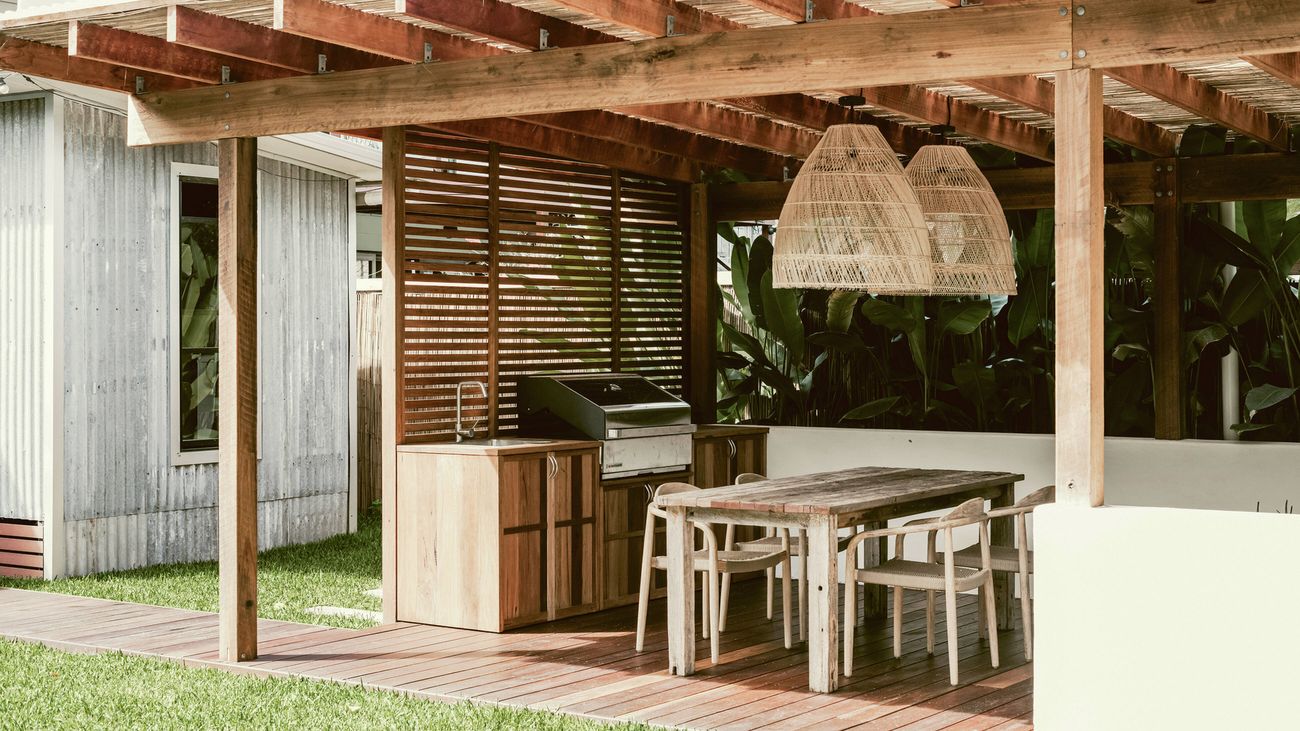 Outdoor barbecue area with wooden cabinetry, dining table, and woven pendant lights under a pergola.