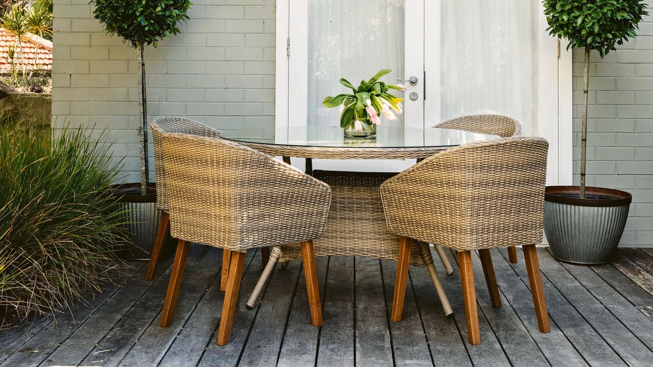 Round outdoor, four seat dining table on a grey timber deck.