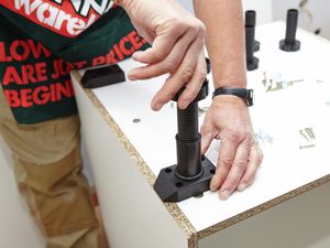 Person attaching a leg to an upside down cabinet