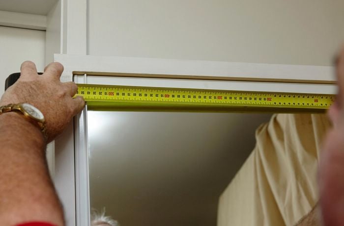 A person measuring the width of a wardrobe mirror door