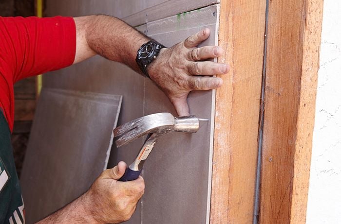 A hole carefully being hammered through villaboard to make room for plumbing lines or electrical cables