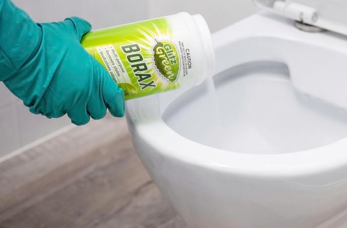 Borax powder being poured into a white toilet bowl