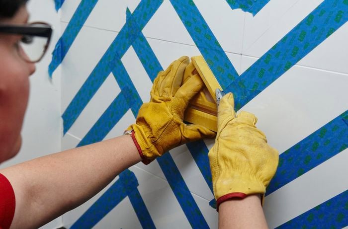 A person using a utility knife and square to trim masking tape on tiles