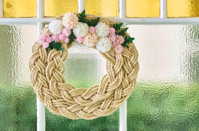 A rope wreath photographed in front of a stained-glass window pane.