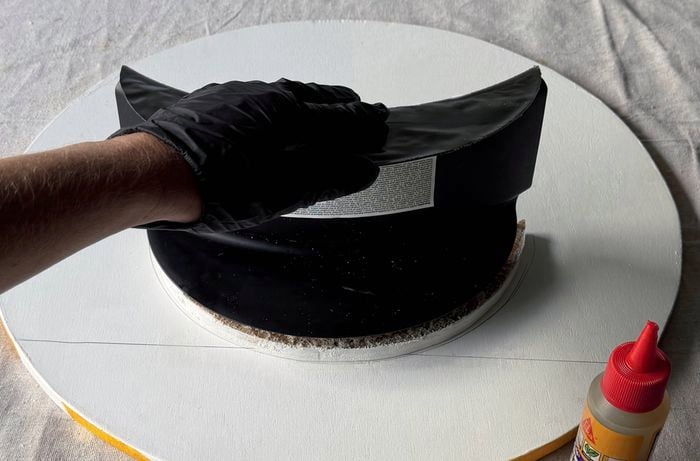 A hand in a black glove attaching a black hose hanger onto a white circular base