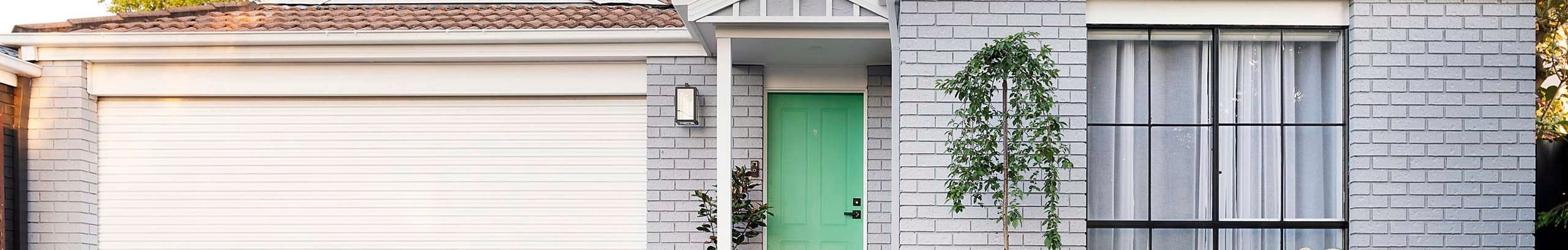 Front of brick house painted grey, with green lawn, neat garden and cricket set.