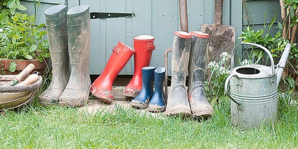 Gardening tools and equipment next to a shed, including gumboots, a shovel, a pitchfork and a watering can.