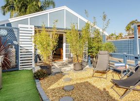 Exterior view of a small blue cottage with white trim, double glass doors, potted bamboo and outdoor seating.